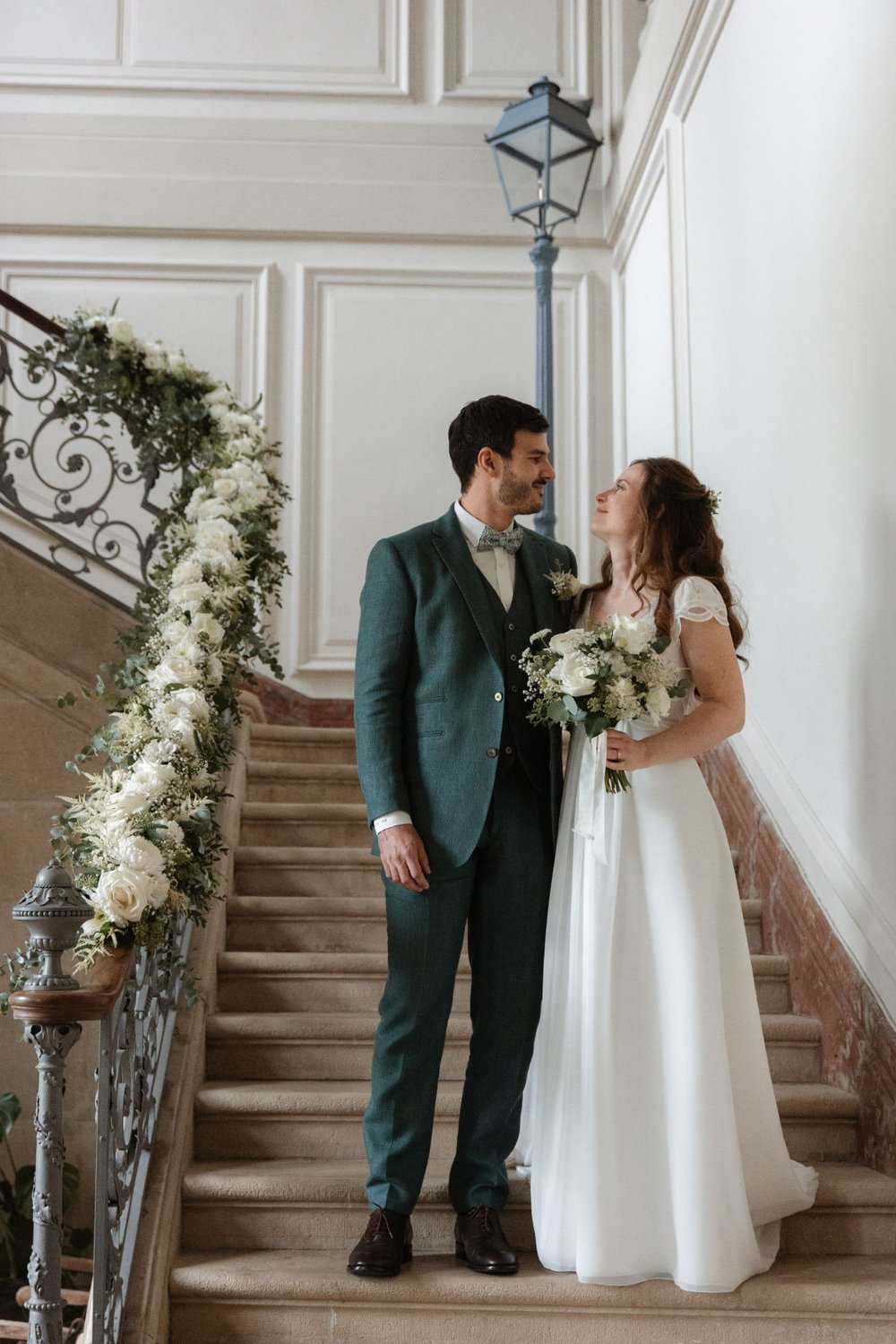 Newlyweds on the château staircase with a white rose garland